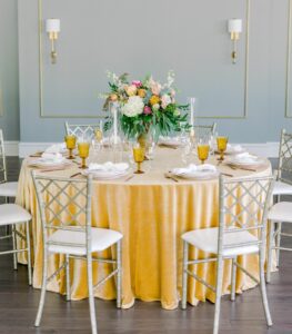 table with yellow table cloth, two charis, flower arrangement